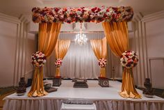 a white table topped with lots of flowers next to a chandelier covered in gold drapes