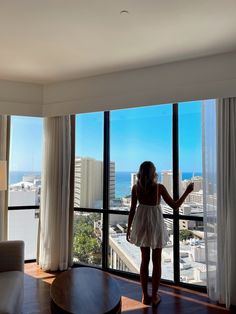 a woman standing in front of a large window looking out at the city below it