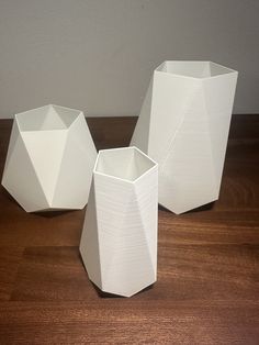 three white vases sitting on top of a wooden table