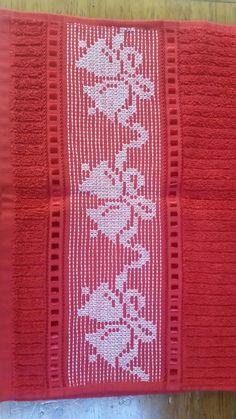 a red knitted blanket with white flowers and leaves on the edge, sitting on a wooden floor