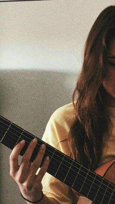 a woman holding a guitar in her right hand and looking down at the strings on it