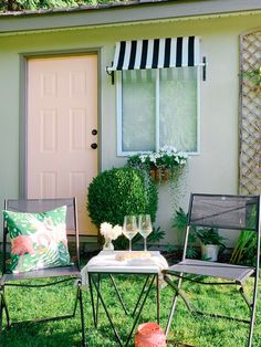 two chairs and a table in front of a house with flowers on the grass outside