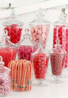 many different types of candies in glass containers on a white table with pink and red candy