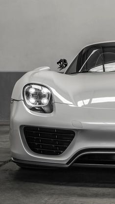 the front end of a white sports car parked in a garage with its hood up