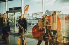 several people are walking through an airport terminal with their luggage and looking out the window