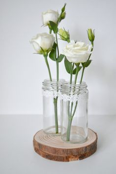 three white roses are in a glass jar on a wooden stand with lace trim around the stems