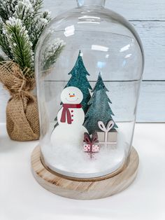 a snowman under a glass clochel with christmas trees in the bottom and presents underneath