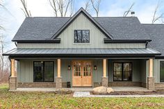 a gray house with black roof and two doors on the front porch, surrounded by trees