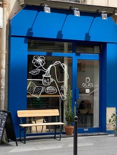 a blue store front with a wooden bench in the foreground and potted plants outside