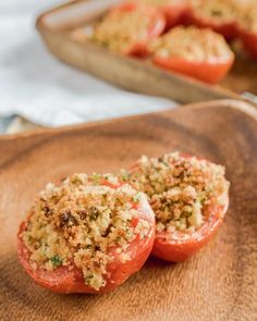 tomatoes stuffed with crumbs sit on a wooden plate next to a baking dish