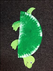 a turtle made out of green paper on top of a black surface with white paint