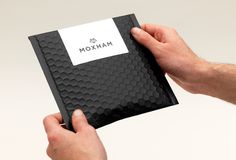 two hands holding a black and white box with the name moxim on it