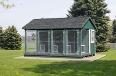 a small green and white dog kennel in the middle of a grassy area with trees