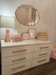 a white dresser topped with lots of drawers and a pink vase next to a mirror