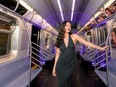 a woman in a black and white polka dot dress standing on a subway train with her arms out