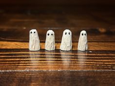 three small white ghost figurines sitting on top of a wooden table next to each other