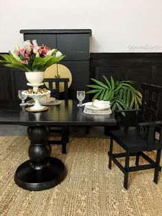 a black table with two chairs and a vase filled with flowers on top of it