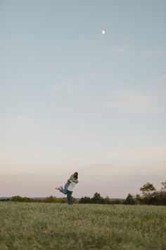 a woman in a field flying a kite at sunset or dawn with the moon behind her