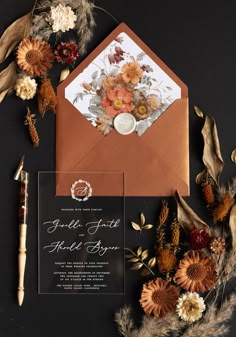 the wedding stationery is surrounded by dried flowers and foliage, including an envelope with a wax stamp