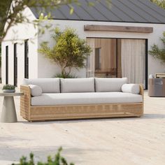 a couch sitting on top of a wooden floor next to a table and bushes in front of a house