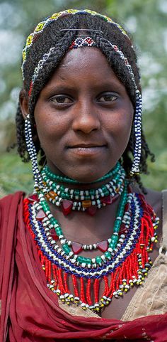 an african woman with beads and necklaces on her head, looking at the camera