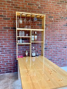 a wooden table in front of a brick wall with bottles and glasses on the shelves