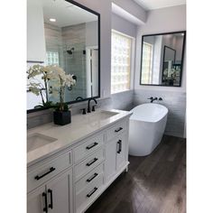 a large white bath tub sitting next to a bathroom sink under two mirrors on top of a wooden floor