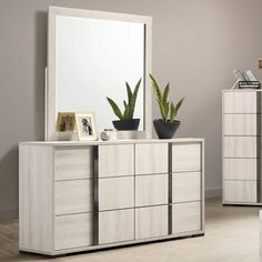 a white dresser sitting next to a mirror and potted plant