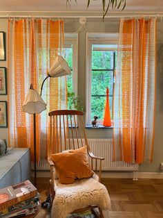 a living room with orange curtains and a chair in front of a window filled with books