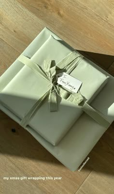 a gift wrapped in white paper and tied with a green ribbon on top of a wooden floor