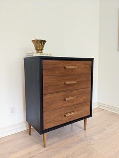 a black and brown chest of drawers on top of a hard wood floor next to a white wall