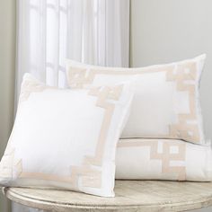 two pillows sitting on top of a wooden table next to a white curtain and window