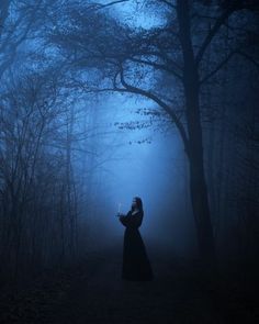 a woman standing in the middle of a forest at night