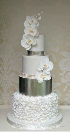 a three tiered wedding cake with white flowers on the top and silver trimmings