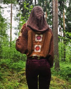 a woman standing in the woods with her back to the camera, wearing a crocheted hoodie