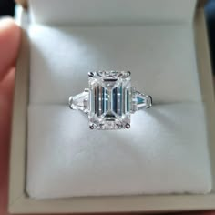 an emerald cut diamond ring with baguettes on the sides in a white box