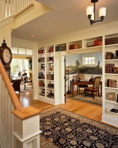 a living room filled with lots of furniture and bookshelves next to a stair case