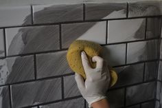 a person in white gloves and rubber gloves cleaning a brick wall with a yellow sponge