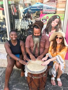 three people are sitting on the sidewalk and one person is playing an african drumming instrument