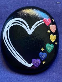 a painted rock with hearts and stars around it on a blue background, in the shape of a heart