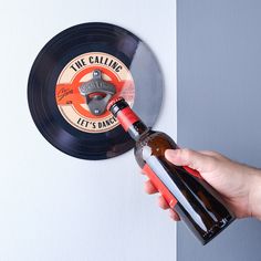 a hand holding a bottle opener over a record wall mounted on a wall next to a vinyl record