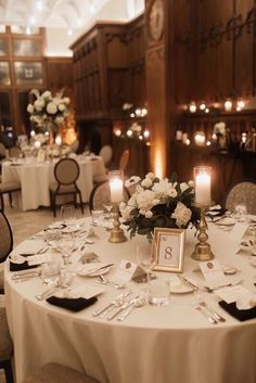 the table is set with white flowers and black napkins, silverware and candles