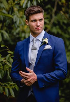 a man in a blue suit and white flowered boutonniere looks at the camera