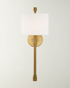 a wall lamp with a white shade on the base and a gold metal frame, against a light gray background