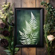 an image of a fern leaf in a frame surrounded by flowers on a wooden table