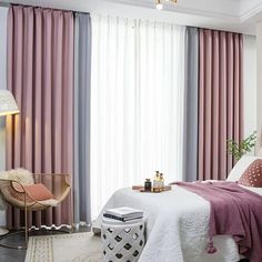 a bedroom with pink curtains, white bedding and a chair in front of the window