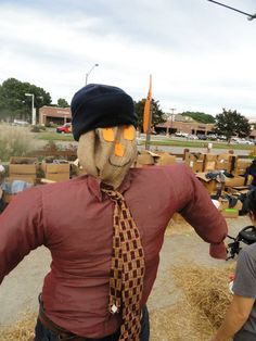 a man in a hat and tie standing next to a scarecrow