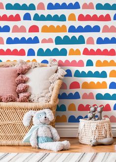 a teddy bear sitting on the floor next to a basket and wallpaper with colorful clouds