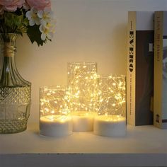 some white candles are sitting on a shelf next to a vase with flowers and books