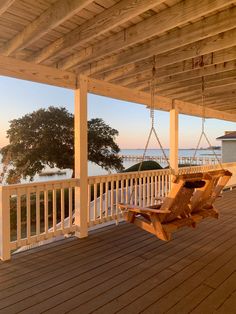 a wooden porch with a swing chair on the back deck and water in the background